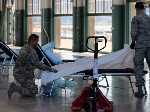 Two men in Army uniforms prepare a hospital bed in Craneway Pavilion.