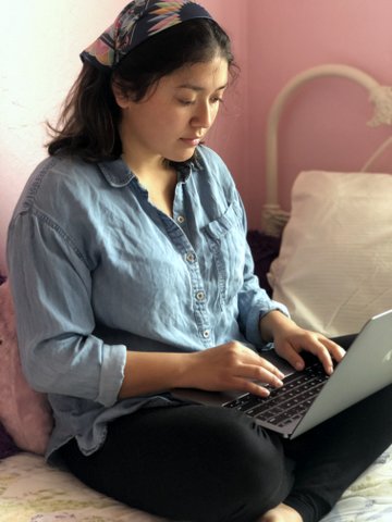 A young woman sits cross-legged on a bed using a laptop.