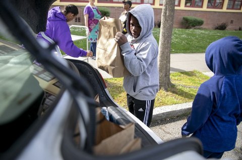 A boy loads a paper sack of food into the trunk of a car.