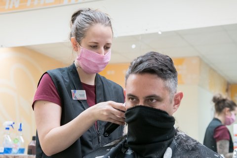 A woman cuts a man's hair with both wearing face coverings.