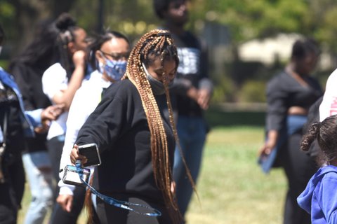 A Black woman in a mask and braids dances in a park.