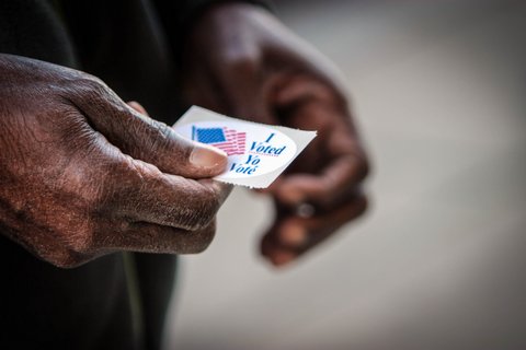 Close-up of a Black man's hands holding an "I Voted" sticker