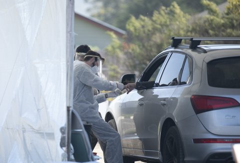 Man in face shield takes finger prick blood sample from hand sticking out of car window.
