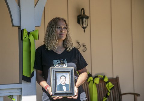 A woman holding a framed photo of her young adult son.