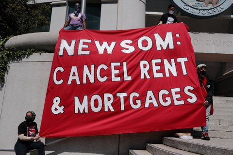 People on steps of government building hold red banner that reads Newsom: Cancel rent & mortgages.