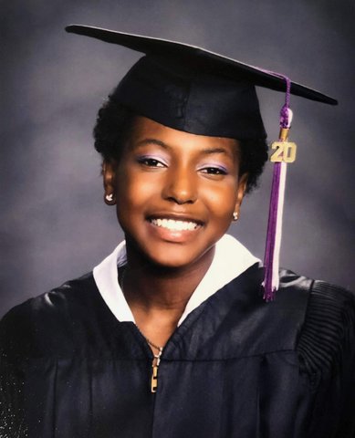 A smiling Black woman in cap and gown with purple and white tassel with the number 20.