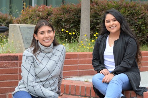 Two smiling young Latina women sitting on brick steps