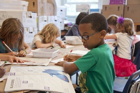 Kids drawing at a table with focus on African American boy in glasses and green shirt.