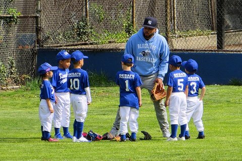 Black man in Yankees cap and Bluebirds Baseball hoodie with kids in baseball uniforms.