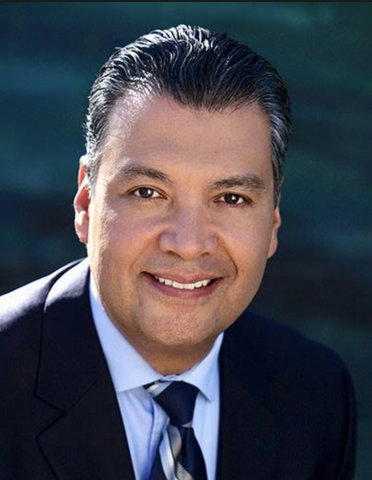 A smiling Latino man in dark suit with tie and light-blue shirt.