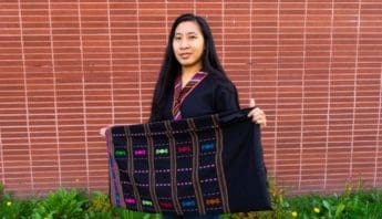 An Asian woman holds a black cloth embroidered with different colors.