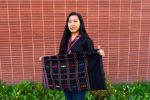 An Asian woman holds a black cloth embroidered with different colors.