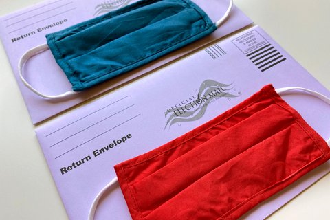 Two purple envelopes that say "Official Election Mail," each with a mask laid on top, one red and one blue.