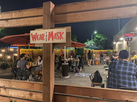 People dining on restaurant patio with sign that says "Wear Your Mask."