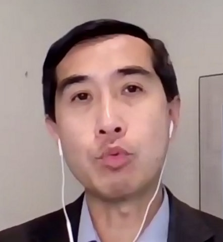 Close-up of an Asian man in a suit with wired earbuds in.