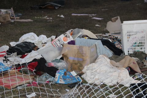 A pile of garbage including a laundry hamper behind a downed chain-link fence.