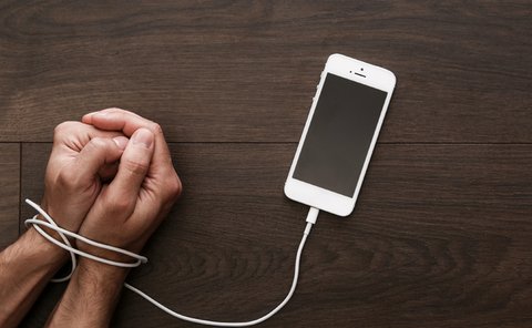 Hands clasped together and bound by a charger cord connected to a smartphone