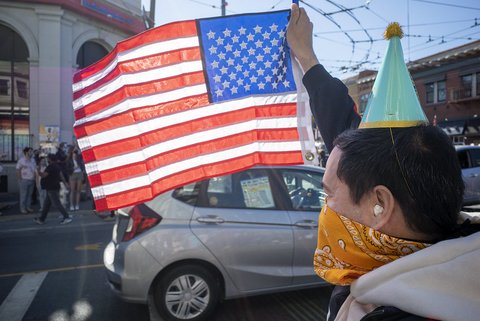 Person wearing a party hat and orange bandana holds up a U.S. flag