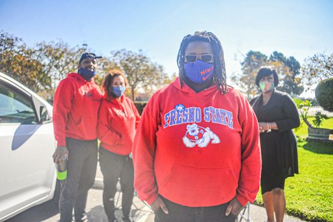 A Black woman in a Fresno state sweatshirt and Nike face mask. A Black man and two Black women are standing behind her.