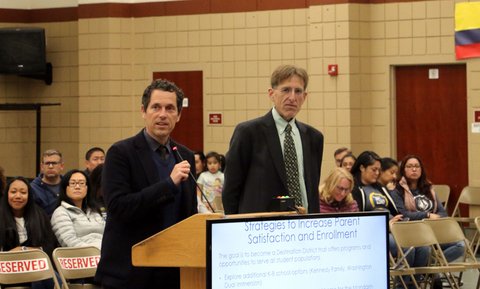 A man at a lectern next to another man in front of people in folding chairs. A screen say "strategies to increase parent satisfaction and enrollment."