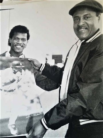 Black-and-white photo of Rickey Henderson and another Black man holding a photo of Henderson running the bases