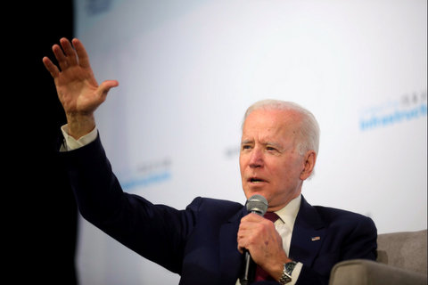 Joe Biden standing with a microphone in his left hand and his right arm outstretched.