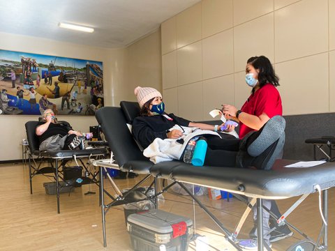 Two people giving blood and a medical worker, all wearing masks.