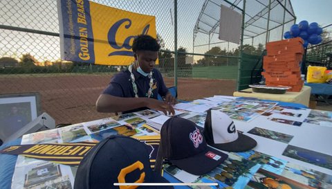 Young Black man at table with photos and ball caps in front of Cal Golden Beats banner