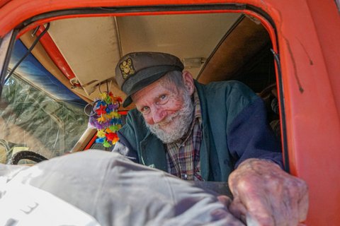 Man with gray beard and sea captain's cap receiving a bundle through the window of his car