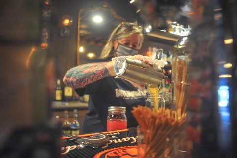 Woman with face mask and tattoo making cocktails.