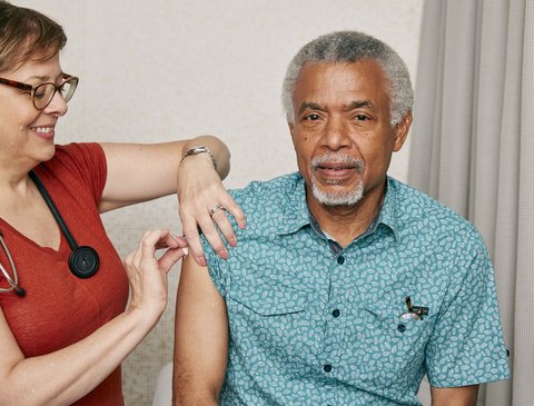 Woman cleaning older Black man's arm before a shot