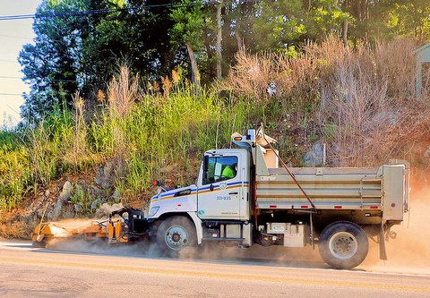 Street sweeping truck driving past hillside