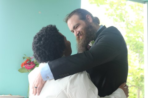 A Black woman and white man standing with their arms around each other, looking into the other's eyes