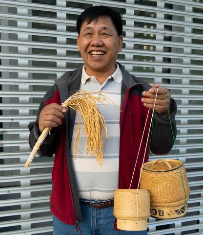 Smiling Asian man holding rice plant and Lao rice baskets.