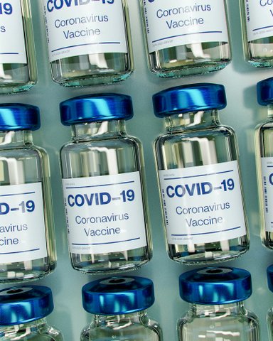 Small glass bottles with blue caps labeled COVID-19 coronavirus vaccine