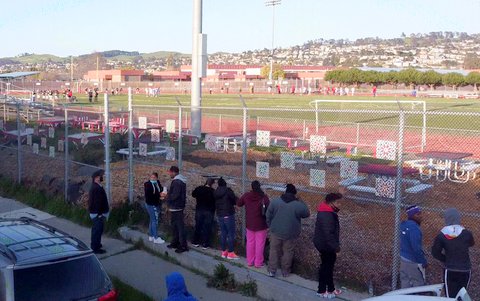 People outside a fenced football field.