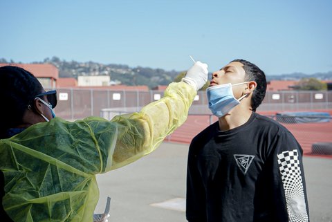 Medical worker swabs the nose of a young man with his mask pulled down.