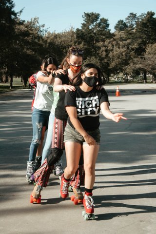 A line of roller skaters each with their hands on the shoulders of the person in front of them.