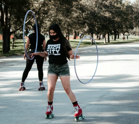 Woman in black Rich City T-shirt and red skates with a hula hoop balanced on each hand.