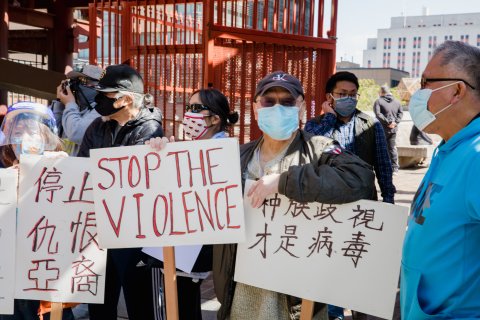 Asian people in masks with one sign that says "stop the violence" and two other signs in Chinese script.