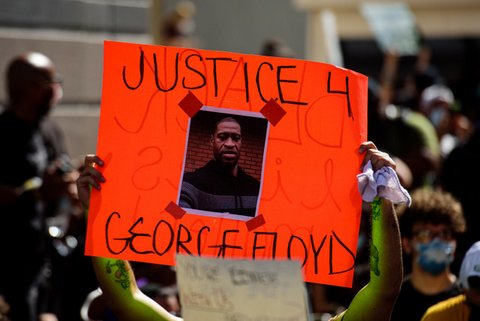 An orange sign with the words "Justice 4 George Floyd" and his picture is held up.