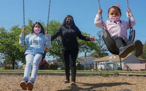 Latina woman pushing her two daughters on swings