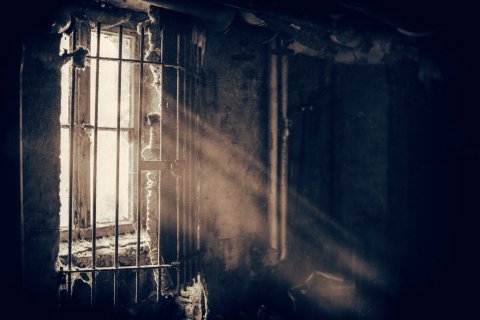 Grayscale photo of sunlight streaming through barred window