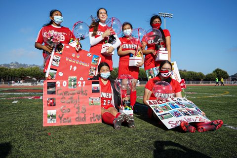 Six young women in red soccer uniforms holding signs, balloons and more.