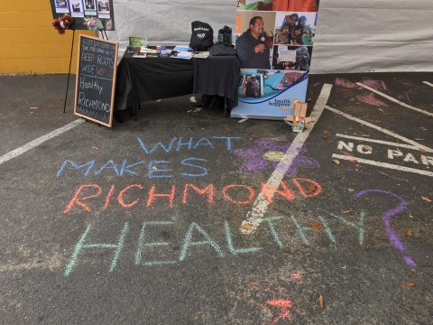 Chalk writing that says "What makes Richmond healthy?" on asphalt in front of a booth