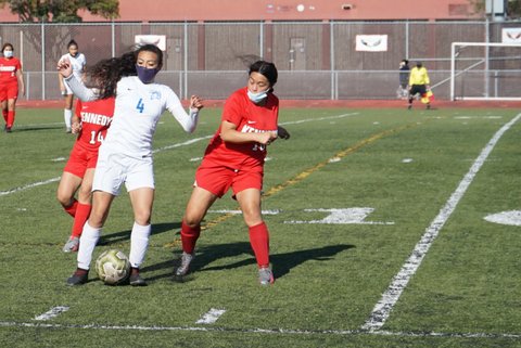 Two girls soccer players going for the ball. Both have masks. One is in red and one is in white.