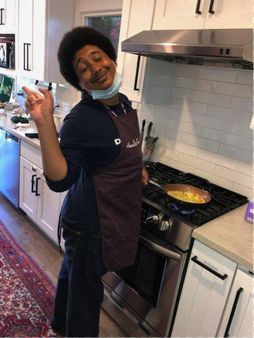 A smiling young Black man in an apron cooking at a stove