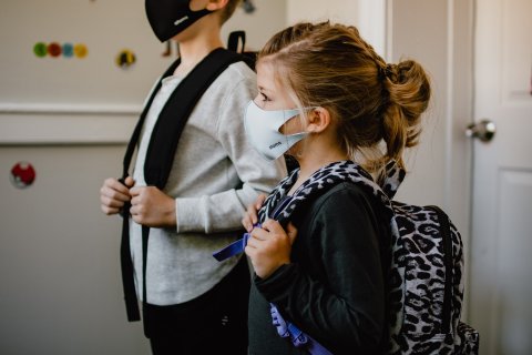 Side view of two kids wearing masks and backpacks