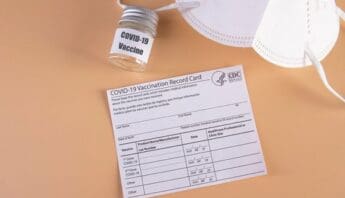 COVID-19 Is Not Going Away A blank COVID-19 vaccination record card, white mask and small jar that says COVID-19 vaccine