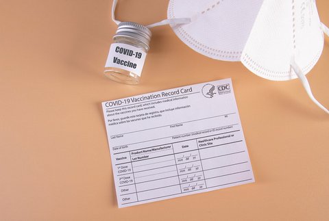 A blank COVID-19 vaccination record card, white mask and small jar that says COVID-19 vaccine